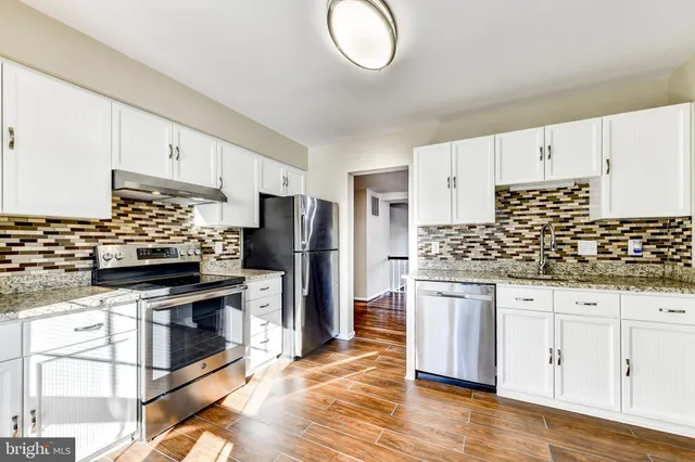 a kitchen with granite countertop a stove a sink dishwasher a refrigerator and a oven with wooden floor