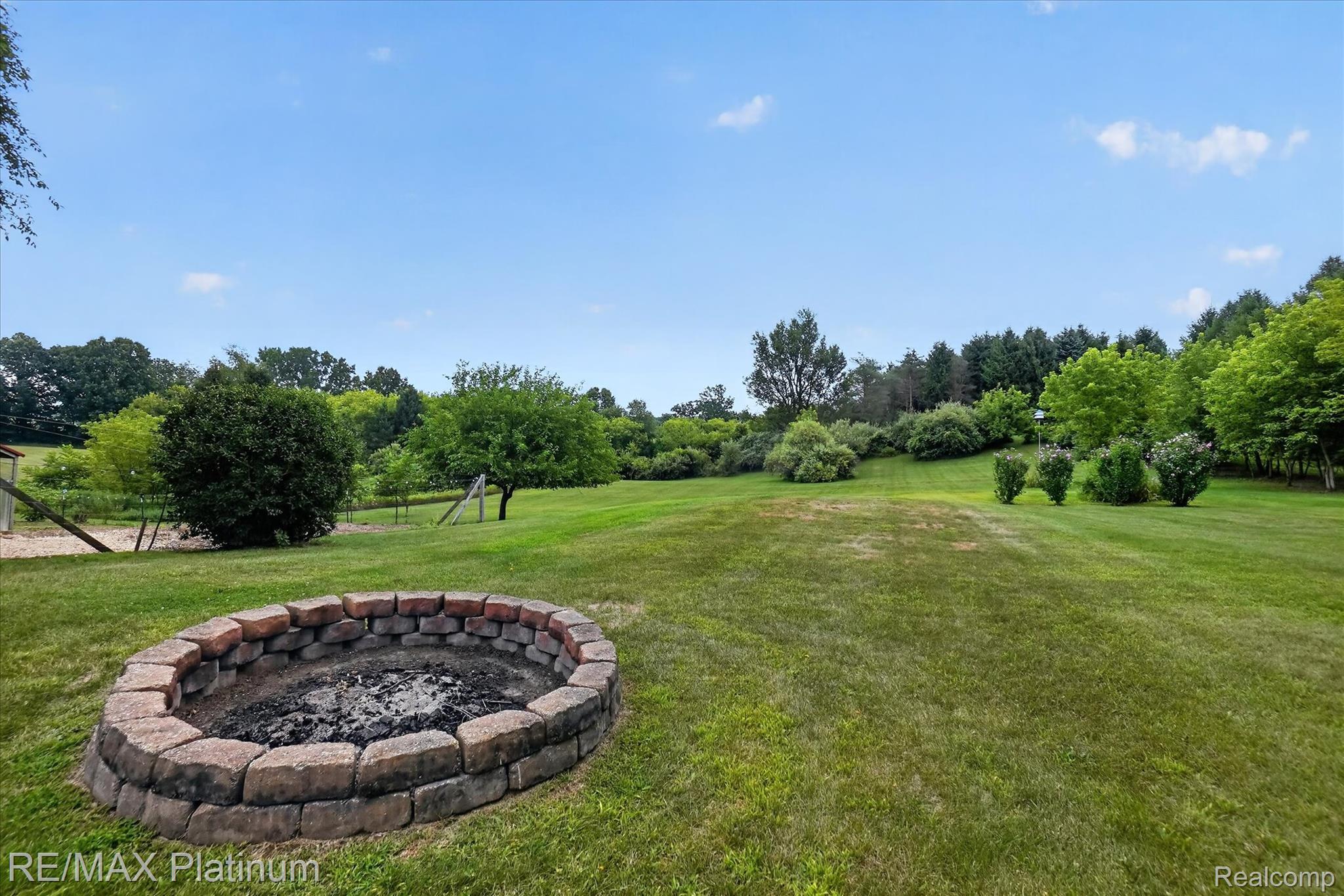 4457 Bradley Road Gregory, MI 48137 - Photo 53 of 79 Expansive green lawn with a built-in stone fire pit, surrounded by mature trees and varied foliage