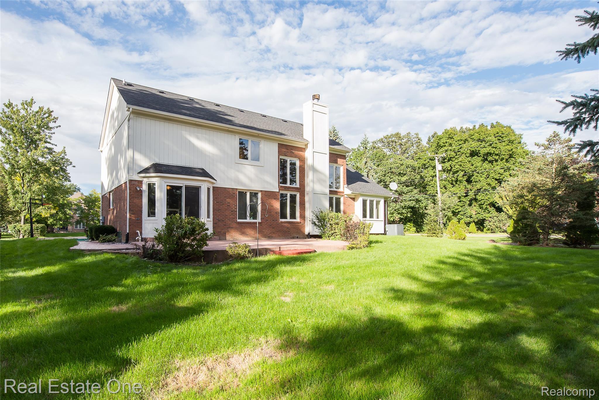 1013 Rochelle Park Drive Rochester, MI 48307 - Photo 63 of 74 Two-story exterior with brick and siding, featuring multiple windows, a bay window, and a rear deck overlooking a spacious lawn