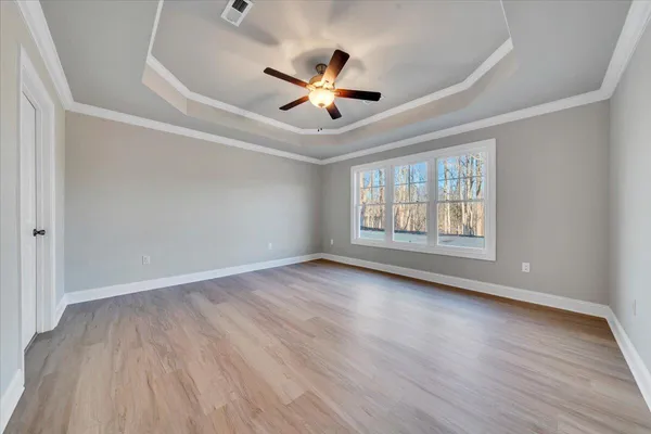 an empty room with wooden floor chandelier fan and windows