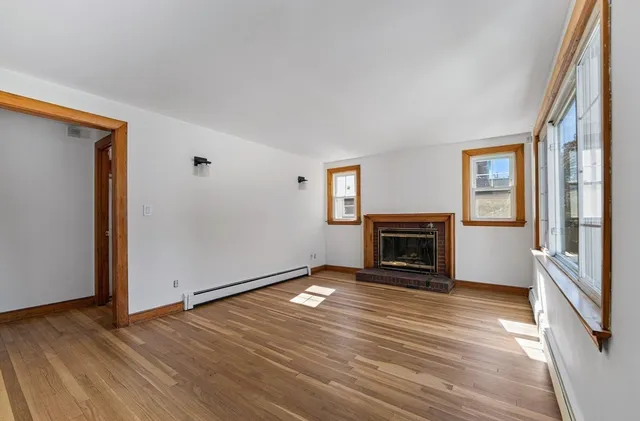 an empty room with wooden floor fireplace and windows