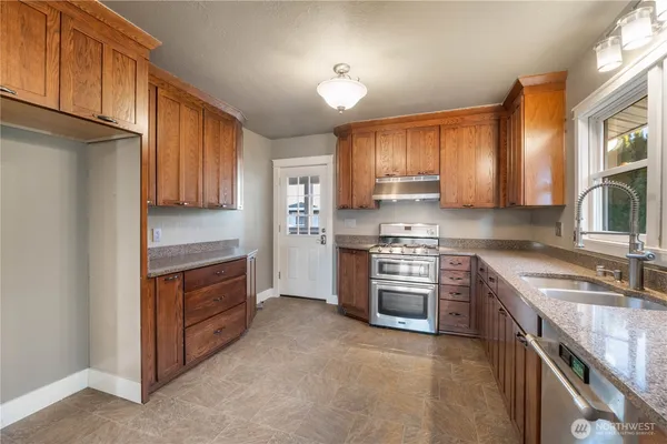 a kitchen with stainless steel appliances granite countertop a stove top oven a sink dishwasher and a refrigerator with wooden cabinets