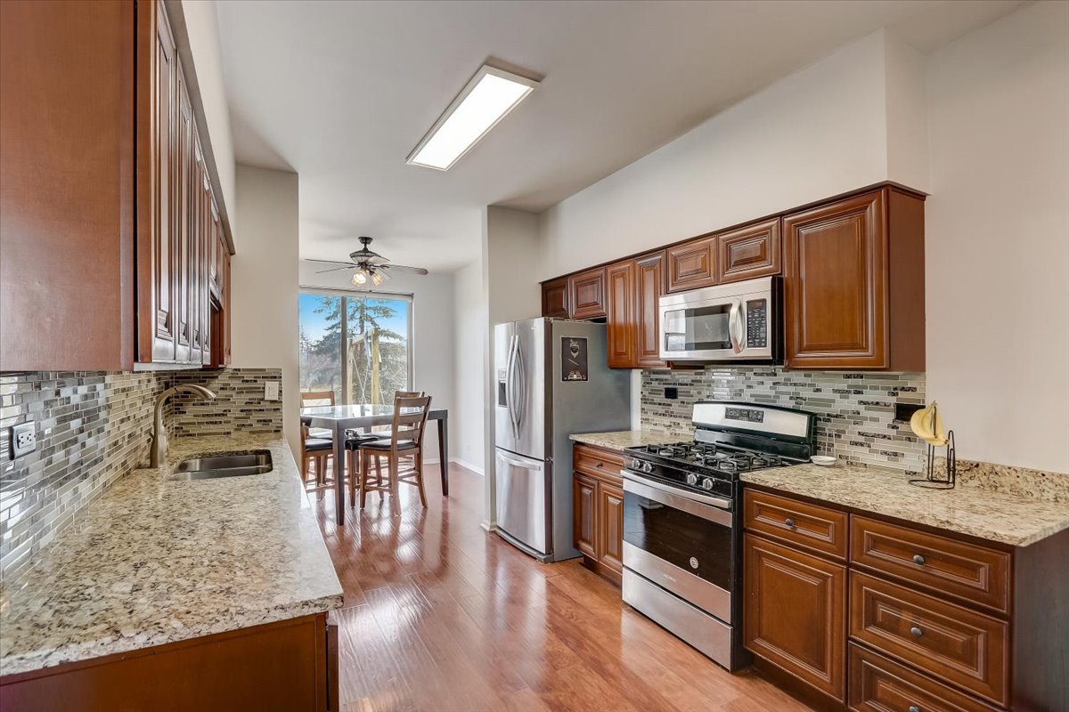 17885 Braewick Road, Unit 17217 Gurnee, IL 60031 - Photo 14 of 35 a kitchen with stainless steel appliances granite countertop a stove top oven a sink a dining table and chairs with wooden floor