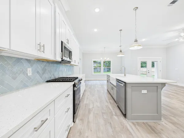 a large white kitchen with kitchen island a stove a sink dishwasher and white cabinets with wooden floor