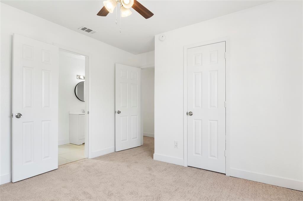 559 Raintree Circle Coppell, TX 75019 - Photo 30 of 40 Carpeted room featuring white six-panel doors, a ceiling fan with light fixture, and an entry to a bathroom with a circular mirror and vanity