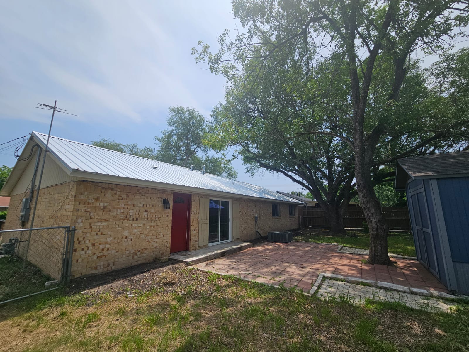 1401 Trinity Street Lockhart, TX 78644 - Photo 30 of 31 Rear exterior featuring a brick facade, white metal roof, and a red entry door
