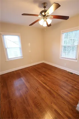 an empty room with wooden floor fan and windows