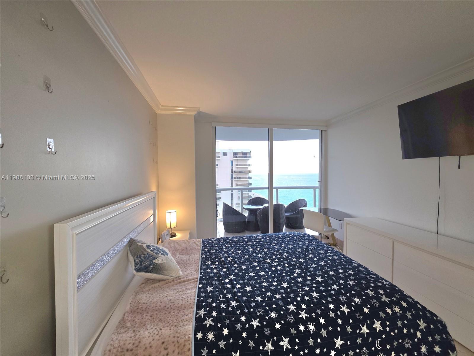 6365 Collins Avenue, Unit 1511 Miami Beach, FL 33141 - Photo 10 of 15 a bedroom with a large bed and a flat tv screen next to a window
