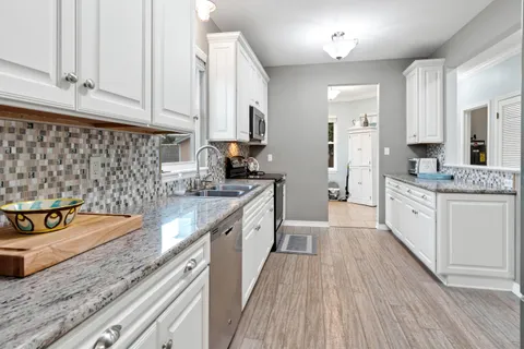 a view of a kitchen with granite countertop a sink dishwasher stove and cabinets with wooden floor