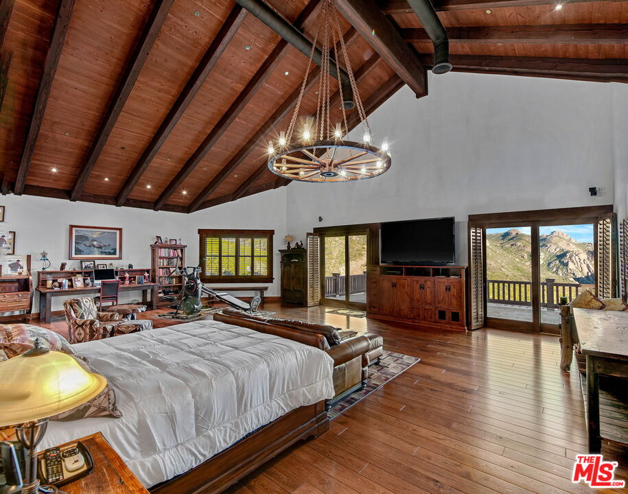 12486 Yerba Buena Road Malibu, CA 90265 - Photo 17 of 68 a spacious bedroom with a bed a chandelier and a flat screen tv