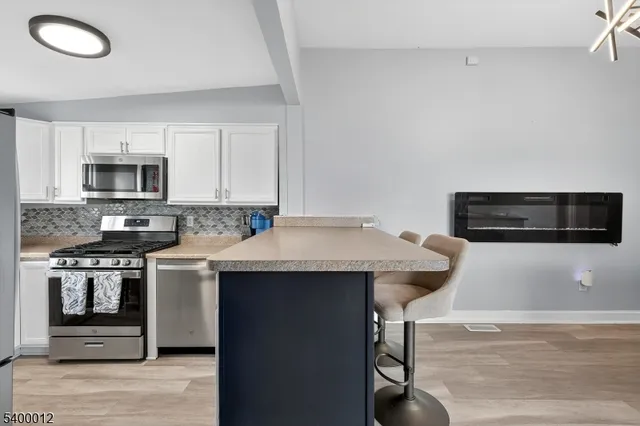 a kitchen with stainless steel appliances granite countertop a refrigerator a stove a sink dishwasher and white cabinets with wooden floor