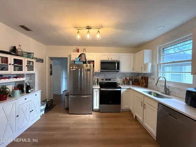 a kitchen with stainless steel appliances kitchen island granite countertop a refrigerator oven a sink dishwasher and white cabinets with wooden floor