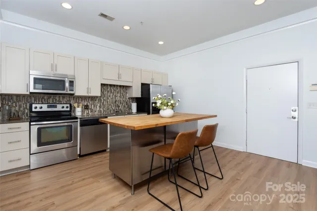 a kitchen with kitchen island a dining table chairs stainless steel appliances and cabinets