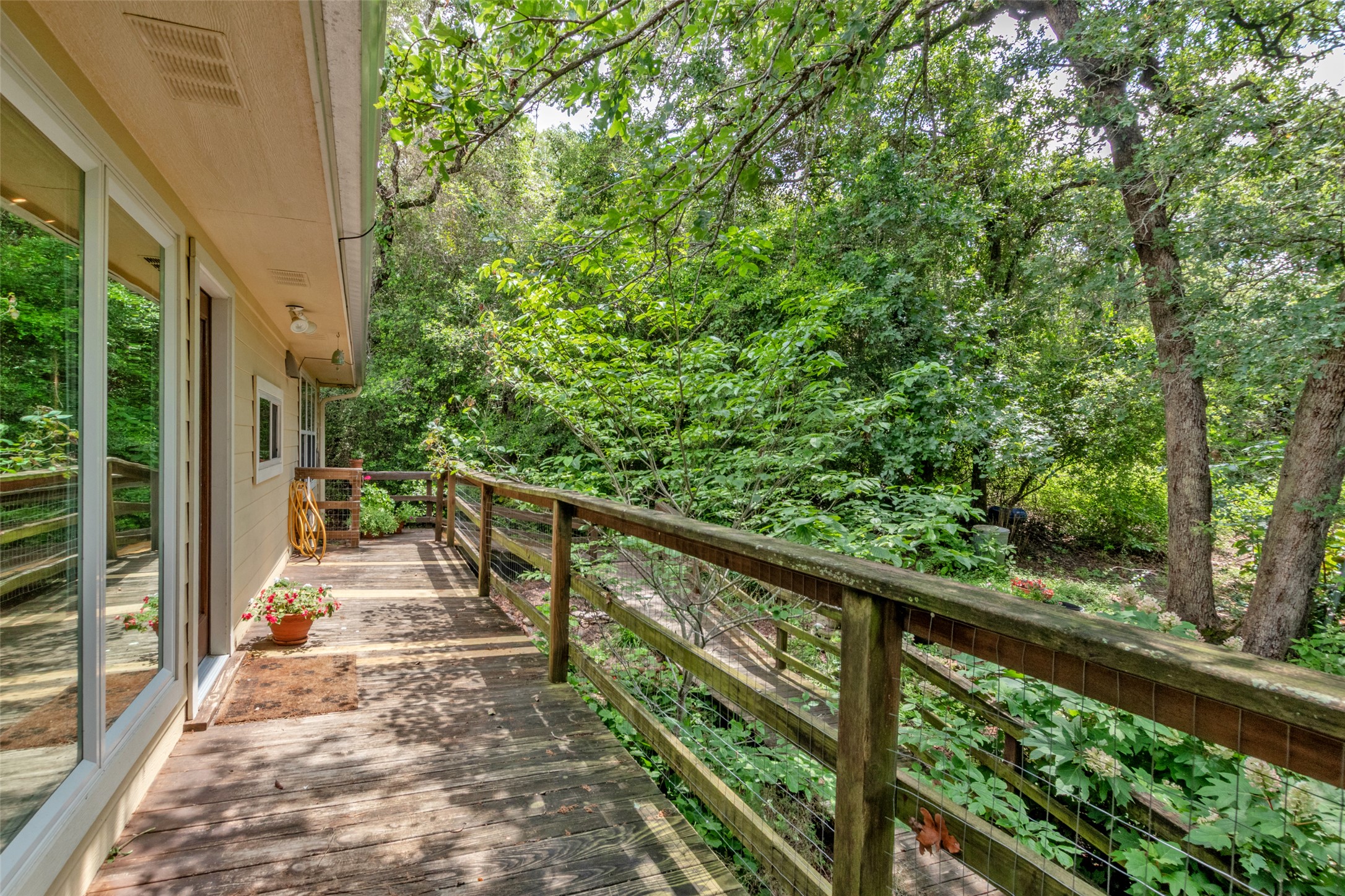 9997 Calhoun Road Bryan, TX 77808 - Photo 2 of 28 Mature trees frame a wooden deck featuring a rustic railing system along the home exterior.