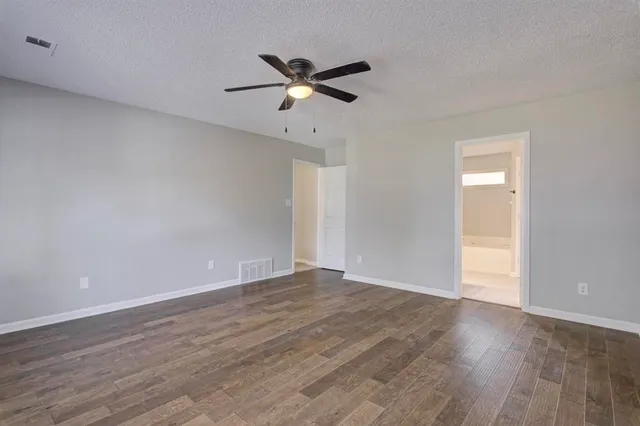 a view of an empty room with wooden floor and a ceiling fan