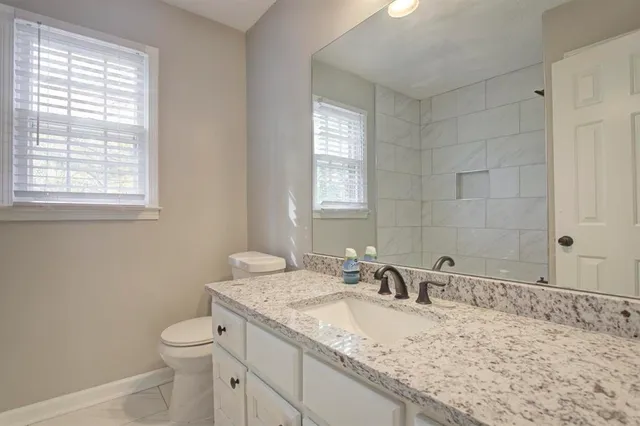 a bathroom with a granite countertop sink a toilet and a window
