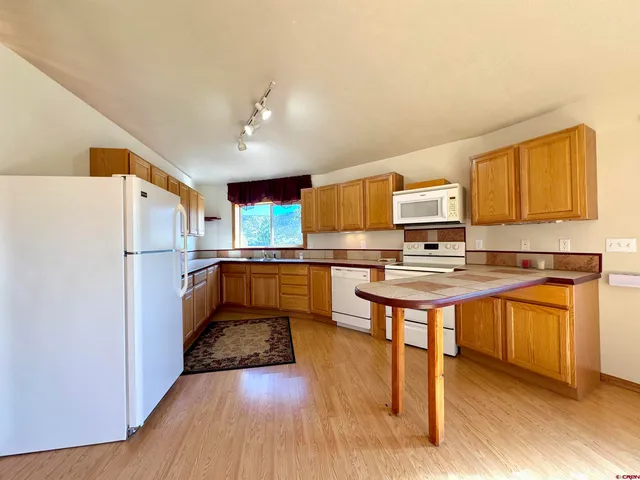 a kitchen with stainless steel appliances a refrigerator a stove a sink dishwasher and a dining table with wooden floor