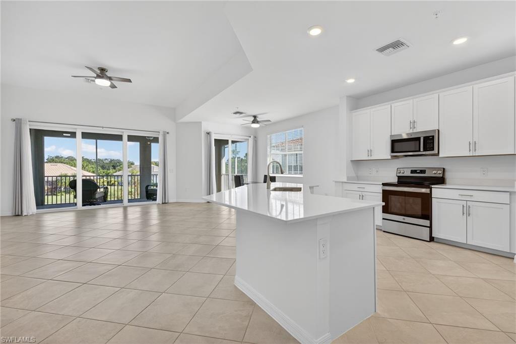 12041 Santaluz Drive, Unit 202 Fort Myers, FL 33913 - Photo 42 of 42 Kitchen featuring stainless steel appliances, white cabinetry, open floor plan, light tile patterned floors, and an island with sink