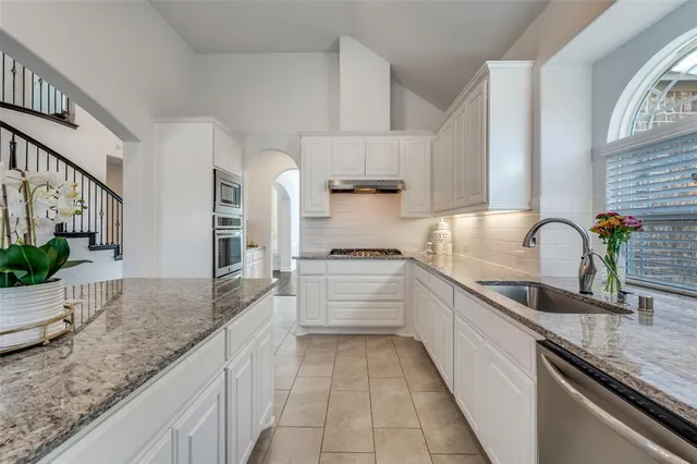 a large kitchen with granite countertop a sink and white cabinets