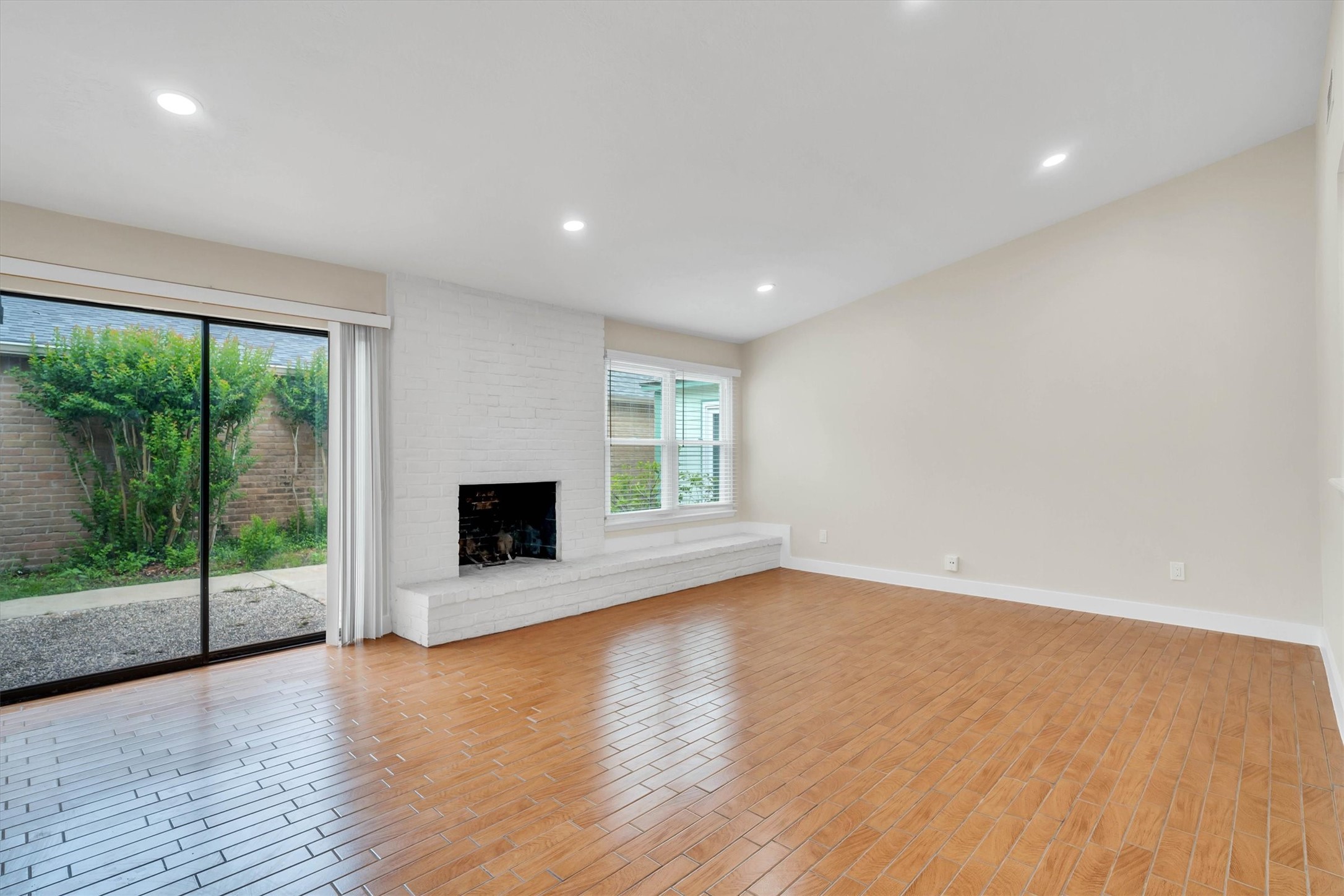 2163 Paso Rello Drive Houston, TX 77077 - Photo 20 of 45 Bright living room with wood flooring, a cozy fireplace, and large sliding glass doors leading to the backyard. Neutral walls and recessed lighting enhance the spacious feel.