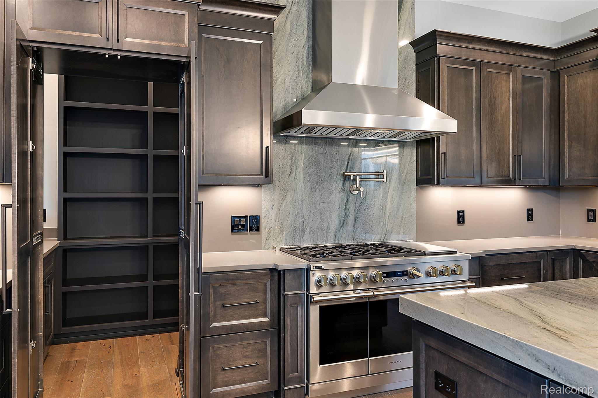 Kitchen featuring dark brown cabinetry, wall chimney range hood, and double oven range