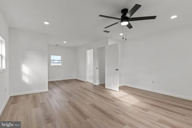 an empty room with wooden floor a ceiling fan and windows