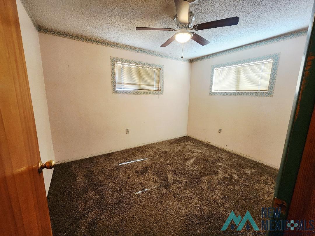 1890 El Portal Road Southeast Deming, NM 88030 - Photo 11 of 21 Empty room featuring dark carpet, ceiling fan, and a textured ceiling