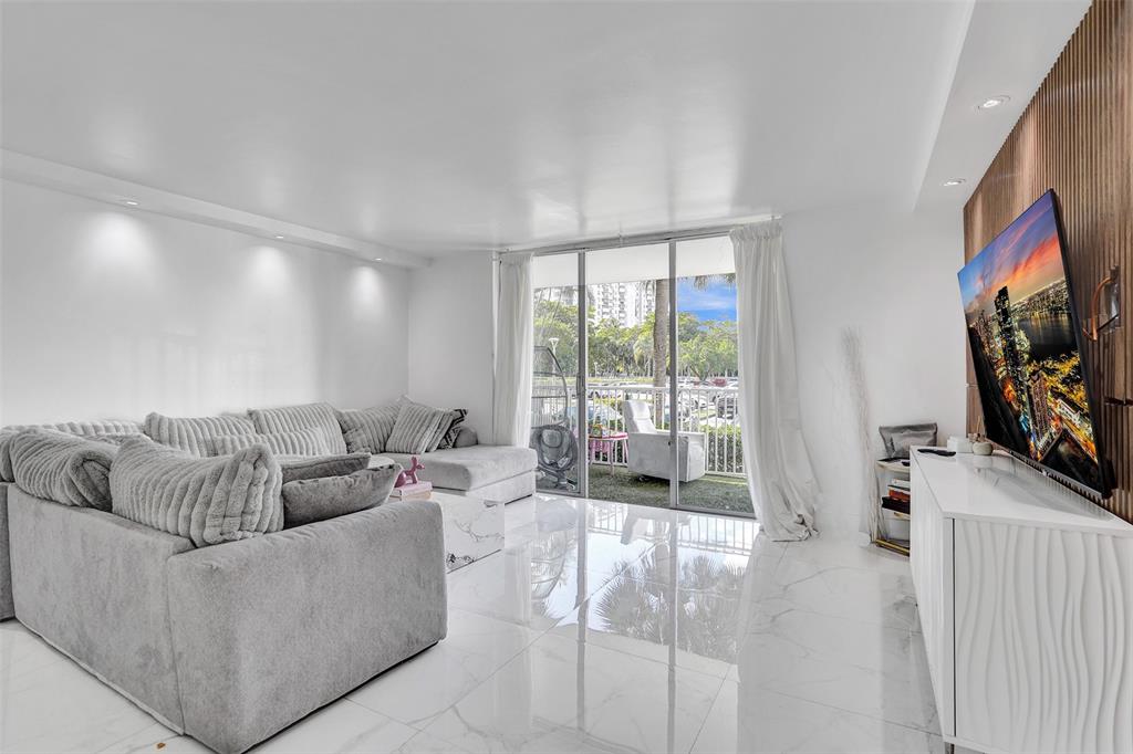 2801 Northeast 183rd Street, Unit 101W Aventura, FL 33160 - Photo 20 of 39 a living room with furniture a flat screen tv and a floor to ceiling window