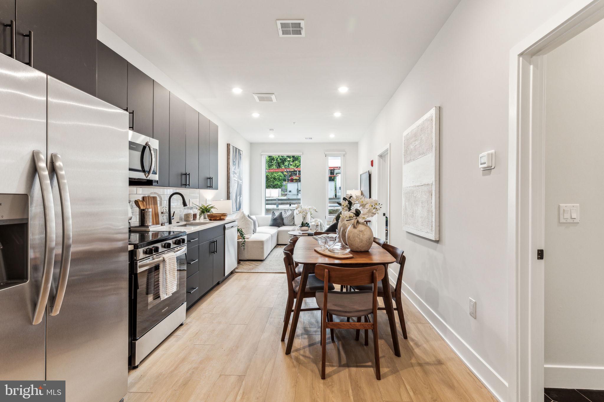 6910 Ridge Avenue, Unit 212 Philadelphia, PA 19128 - Photo 5 of 18 a kitchen with stainless steel appliances kitchen island granite countertop a refrigerator a stove a sink dishwasher a dining table and chairs with wooden floor