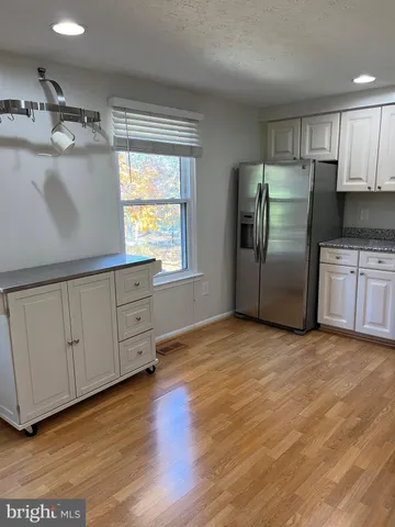 a kitchen with stainless steel appliances granite countertop a refrigerator a sink and white cabinets with wooden floor