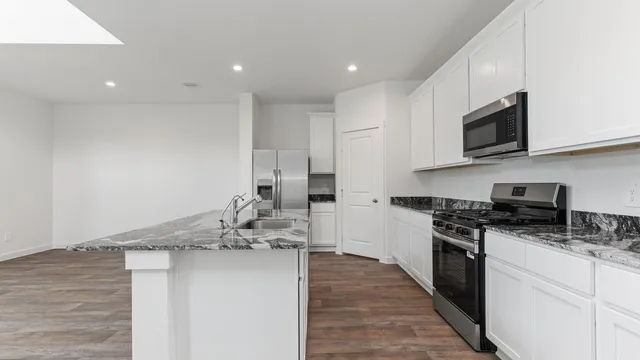 a kitchen with stainless steel appliances kitchen island granite countertop a stove top oven a sink a counter space and cabinets