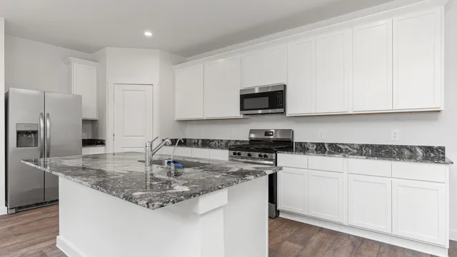 a kitchen with stainless steel appliances granite countertop a sink a stove a microwave a sink a refrigerator white cabinets and a wooden floor