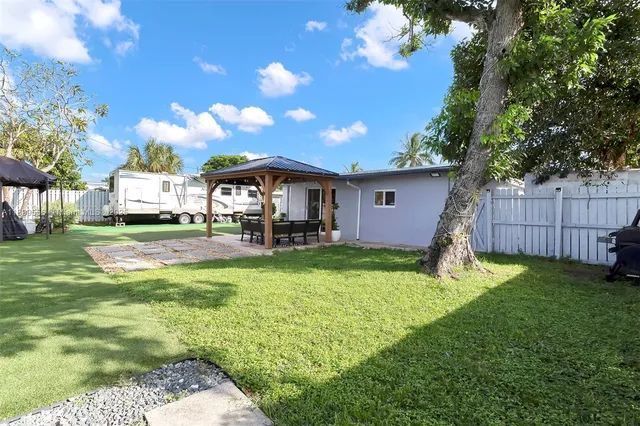 a view of a white house with a yard potted plants and large tree