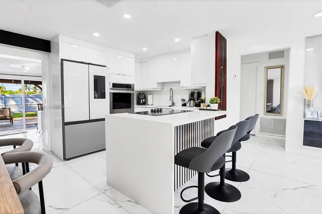 a kitchen with stainless steel appliances kitchen island granite countertop a refrigerator a stove a microwave oven a sink with island chairs and couches with wooden floor