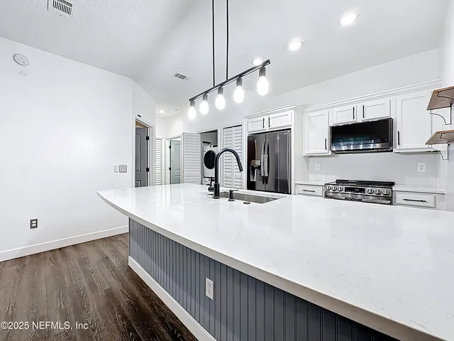 a large kitchen with stainless steel appliances a large counter top a stove and a sink