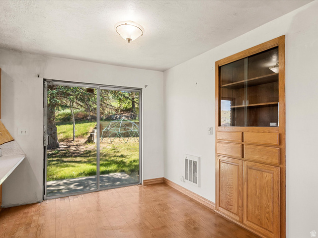 15680 North Beaver Dam Road Collinston, UT 84306 - Photo 11 of 49 Sliding glass doors opening to outdoor space, wood-finish flooring, built-in wooden cabinet with glass-front display, overhead semi-flush mount lighting, and white wall finishes