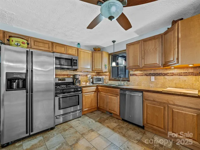 a kitchen with stainless steel appliances granite countertop a refrigerator a sink dishwasher a stove top oven a kitchen island and chairs with wooden floor