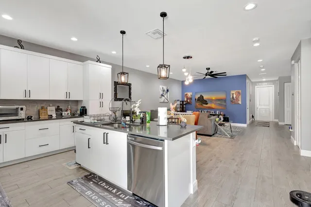 a kitchen with stainless steel appliances kitchen island granite countertop a stove a sink a refrigerator and white cabinets with wooden floor