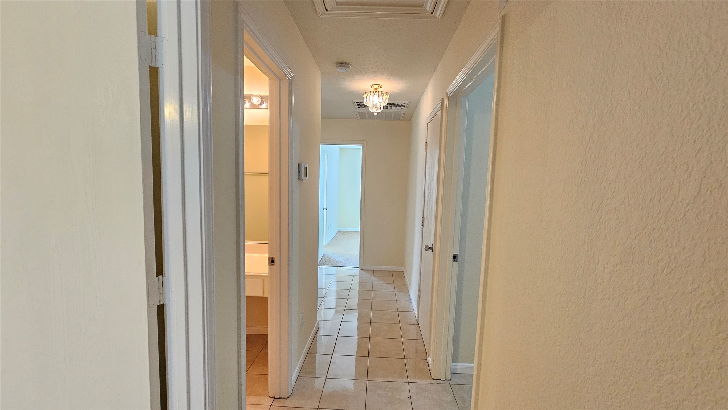 7918 Barnes Ridge Lane Houston, TX 77072 - Photo 10 of 34 Bright hallway with tiled flooring, featuring multiple doors leading to different rooms. A chandelier adds elegance, and a glimpse of natural light enters from the far end.