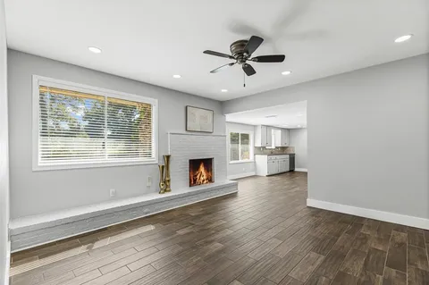 a view of a livingroom with a fireplace a ceiling fan and wooden floor