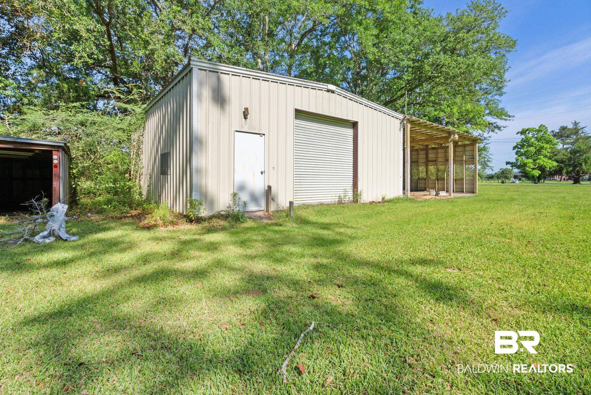 18318 Kendrick Road Robertsdale, AL 36567 - Photo 24 of 39 Metal-sided structure featuring a large roll-up door, pedestrian entry, and an attached covered lean-to