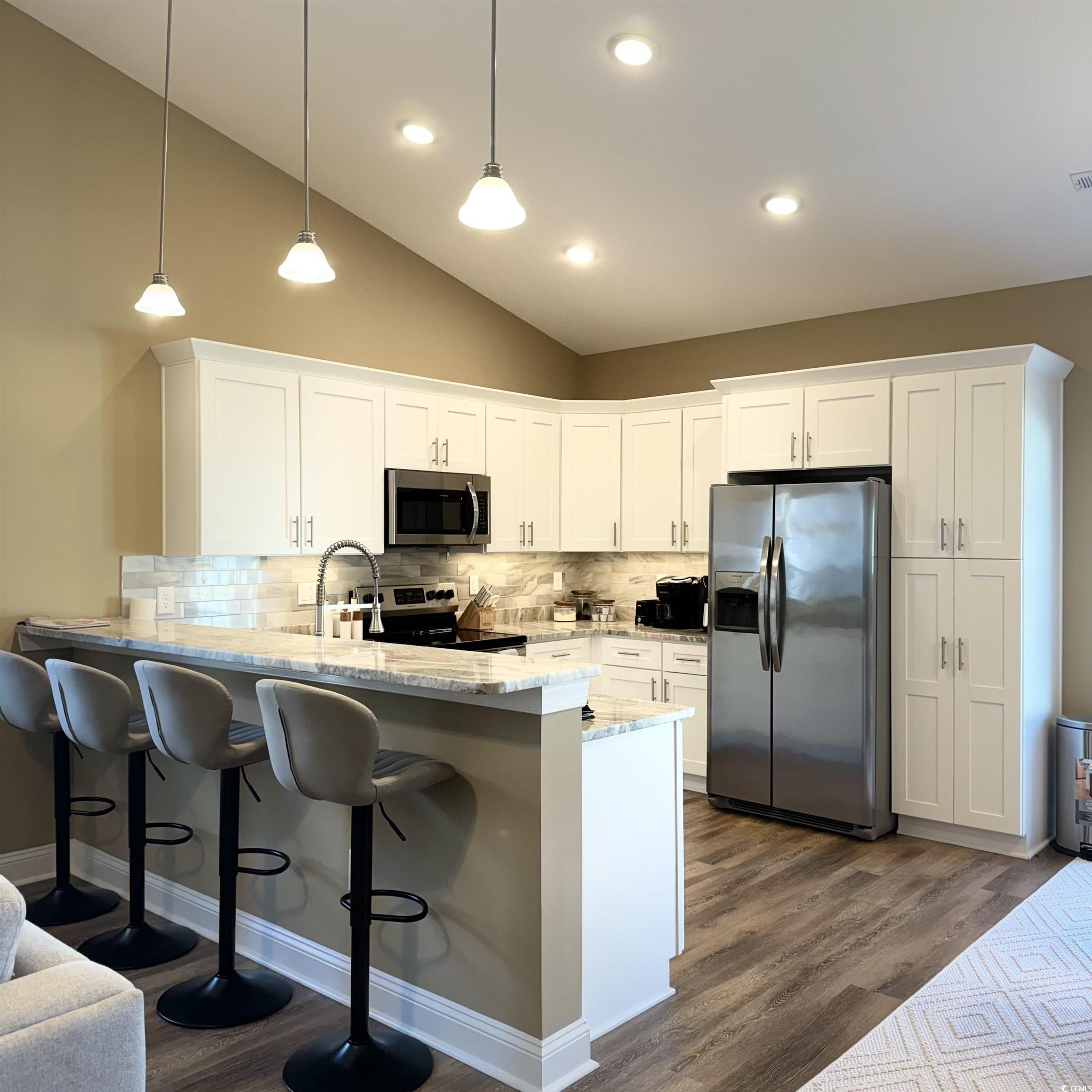 633 11th Avenue South Myrtle Beach, SC 29577 - Photo 6 of 25 Kitchen with a kitchen bar, stainless steel appliances, a peninsula, light stone counters, and white cabinets