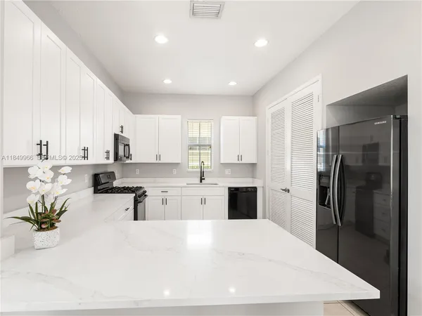 a large white kitchen with a refrigerator a stove a sink a dining table and chairs