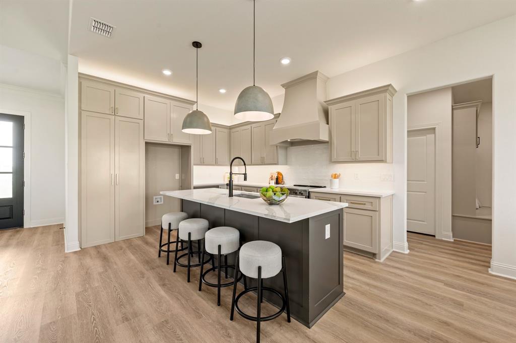 2705 Gospel Road Tolar, TX 76476 - Photo 11 of 36 Contemporary kitchen featuring light luxury vinyl flooring, a central island with a white countertop and seating, custom cabinetry, recessed lighting, and a built-in range hood