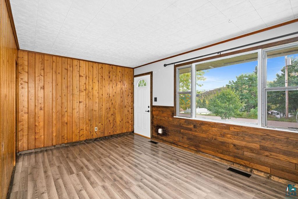 66 Banks Boulevard Silver Bay, MN 55614 - Photo 5 of 19 Empty room featuring wood walls, ornamental molding, wood finished floors, and a wainscoted wall
