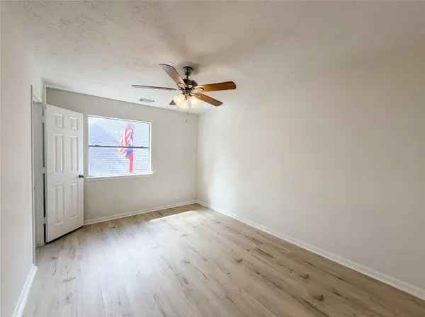an empty room with wooden floor fan and windows
