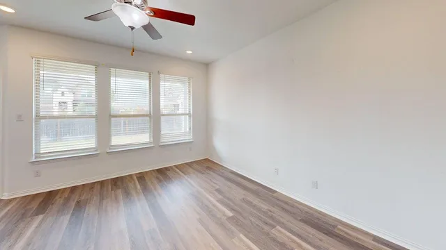 an empty room with wooden floor chandelier fan and windows