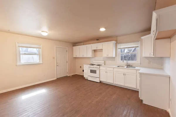 a large kitchen with granite countertop a stove top oven a sink a dining table and chairs with wooden floor