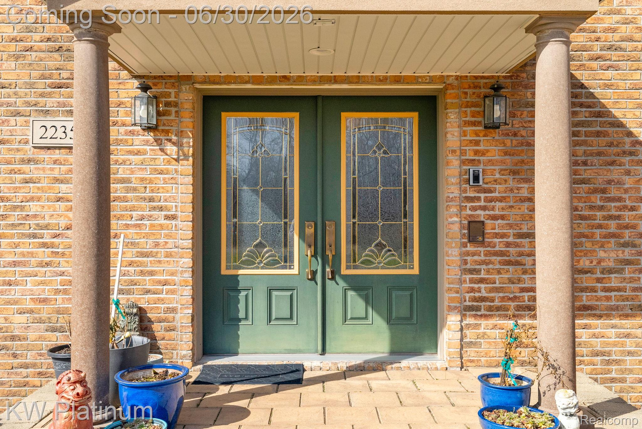 2235 South Lake Shore Road Harbor Beach, MI 48441 - Photo 4 of 99 Brick facade entry featuring double green doors with decorative leaded glass inserts, flanked by two stone columns, under a covered portico with exterior lighting