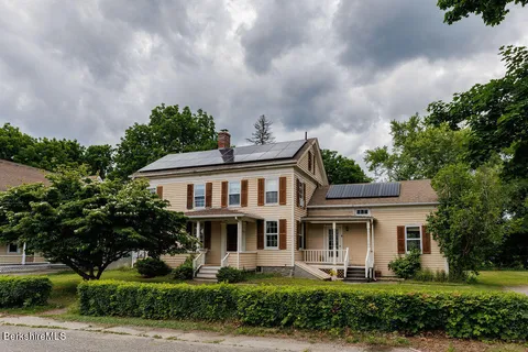 a view of a white house with a big yard and potted plants and large trees